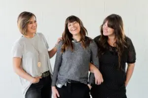 Three women smiling and standing in front of a white wall.