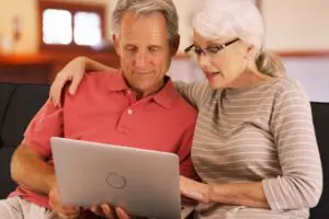 A mature man and woman sitting on the couch doing an internet search on their laptop for liposuction and alzheimers disease.