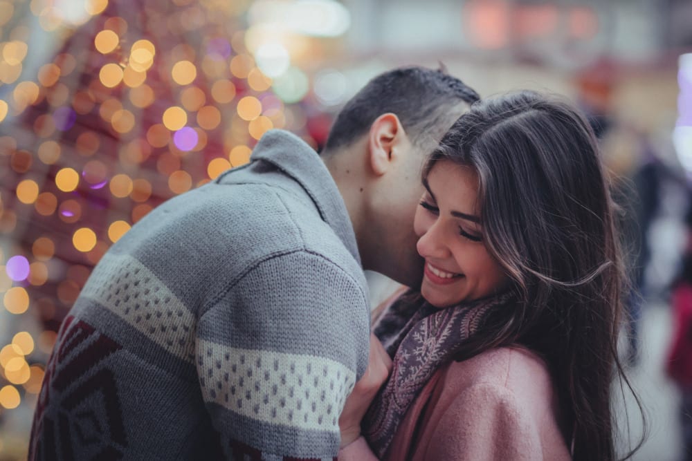 Man and woman embracing in front of holiday lights