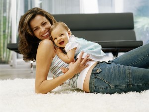Baby girl (6-9 months) sitting on reclining mother, laughing, portrait