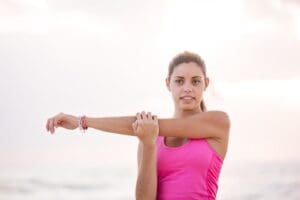 Woman in pink tank top stretching arm.