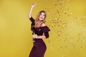 Woman in burgundy dress throwing confetti in celebration.